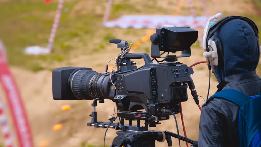 Operator Cleans Lens Of Professional Videocamera, And On Background 