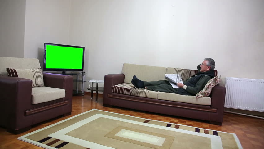 Senior Man Watching TV Show While Sitting On Sofa In His Living Room