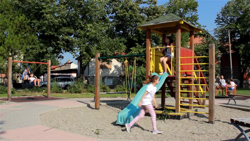 Children Playing In The Park. Young Girls Going Down On The Slide