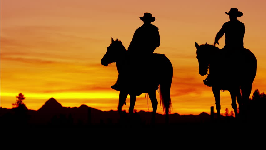 Dusk Shot Of Four Cowboys Riding Off Into The Sunset Towards Mountains ...